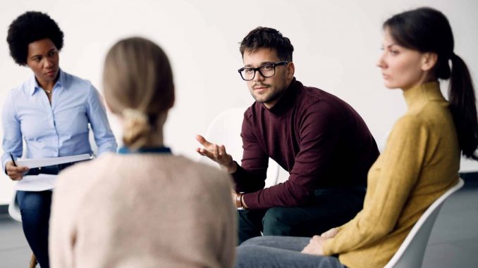 Young man communicating with participants of group therapy at co