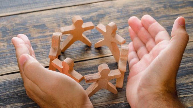Business success concept on wooden background high angle view. hands protecting wooden figures of people.